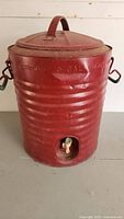 Front view of the red metal exterior water cooler with lid and spigot.