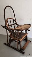Front angle showing antique wooden high chair with curved backrest and detachable tray on top, made of sturdy wood with visible wear.