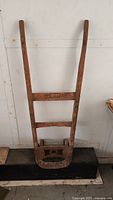 Full front view of the antique wooden and metal dolly showing the long handles and base.