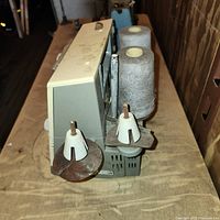 Side view showing spool holders with two large gray thread cones attached to the machine.