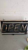 Front view of the neon "OPEN" sign with black backing and visible neon tubing spelling 'OPEN'.