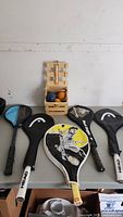 Four sports racquets with black protective covers and a wooden crate bocce ball set on table, showing overall content of the lot