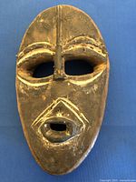 Front view of the oval hand-carved wooden mask with geometric facial details and accentuated white markings.