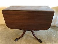 Side view of antique wooden drop leaf table showing classic claw foot base and closed leaves