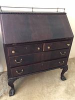 Front view of closed drop-front desk showing drawers, brass hardware, rope-twist edge and claw feet