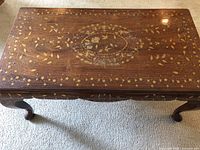 Top view of the antique wooden inlay table showing detailed floral and ornate patterns in gold and light colors on a rich brown wood background.