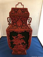 Front view of tall red cinnabar lacquer vase with floral carvings and green background.