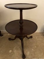 Full view of two-tier wooden table showing smaller upper round top and larger lower round shelf, dark brown finish, central supporting column, and claw foot legs.