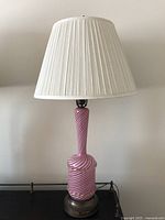 Full view photo showing the lamp with the white pleated lampshade and Murano glass body in pink and white spiral stripes on a metal base.