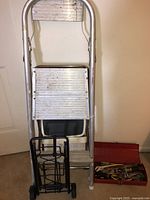 Aluminum stepstool, black folding luggage cart in front, and red metal toolbox on the floor