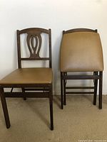 Pair of two brown wooden folding chairs with tan leatherette cushions shown from front and back, on a white background.