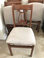 Front view of a wooden folding chair with beige dotted upholstery and lyre back design.