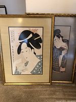 Two framed Japanese Ukiyo-e prints leaning against wall on carpeted floor
