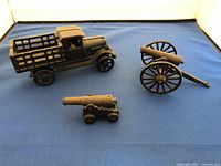 Overview of the three cast iron collectible models shown on blue fabric background under soft light. Includes the model truck and two cannon models.