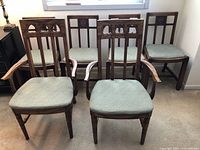 Six vintage dining chairs, including two captain chairs with armrests and four standard chairs without armrests. Chairs have wooden frames and green padded seats.