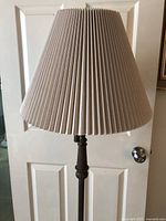 Close-up view of the pleated beige lampshade and top portion of the dark metal floor lamp