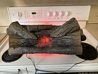 Electric fireplace log set resting on stove top, showing multiple synthetic logs with incandescent flame effect glowing red inside.