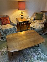 Photo showing the coffee table in a living room setting with two chairs and a lamp.