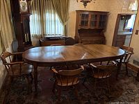 View of oval extendable dining table with two leaves attached and six surrounding chairs in a room with carpet and curtains.