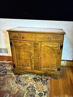 Full front view of the wooden buffet showing two drawers and double doors with metal knobs and black hinges, wood grain finish.