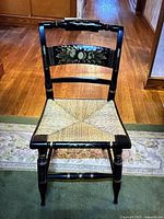 Front view of L. Hitchcock vintage black chair with woven seat and gold hand-painted details on backrest and legs.