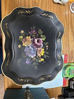 Full view of black metal tray with colorful hand-painted flowers and gold accent designs along the edge.