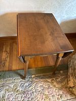 Rectangular wooden side table from a front corner angle showing the top surface and legs against wall and floor.