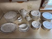 Image showing entire porcelain set arranged on countertop including multiple plates of different sizes, tea pot, sugar bowl, cream pitcher, gravy boat, and serving plates.