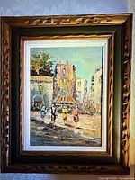 Frontal view of the small framed oil painting showing impressionist street scene with people and buildings under blue sky