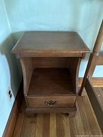 Front angle view of the brown wooden nightstand showing its drawer, open shelf, and curved sides.