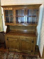 Overall front view of the traditional style wooden hutch cabinet showing glass upper doors and lower wooden doors with drawers.