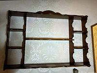 Front view of the brown traditional wooden wall shelf mounted on a wall with multiple shelves and decorative edges.