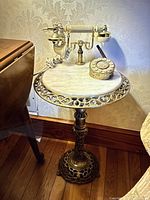 Full side view of antique telephone on marble-topped brass stand.