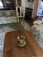 Full view of vintage brass fireplace tool set with four tools on wooden table, showing polished brass finish and cylindrical handles.