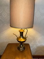 Full view of the vintage brass gold table lamp with beige fabric shade emitting light