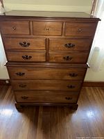 Front view of the vintage brown wooden chest of drawers with visible metal handles and drawers.