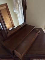 Close-up of the open drawer below the mirror showing the wood interior and brass drawer pulls.