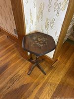 Vintage wooden accent table corner showing the dark wood top with painted fruit pattern and four-legged base on hardwood floor.