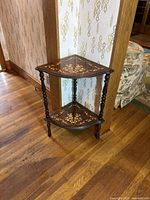 Full view of the vintage 2-tier corner table showing the dark brown wood, floral inlay design on both tiers, and turned legs.