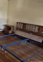 Full view of vintage king bed frame showing headboard with carved decorative panels and spindles, metal frame base on wheels, and one nightstand visible