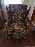 Front view of the vintage wingback chair upholstered in a multi-color pastoral scene fabric showing the full structure, arms, back, and skirt.