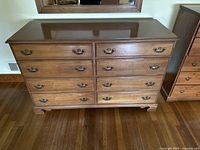 Full front view of vintage wooden dresser showing all drawers and metal handles, positioned in a room with hardwood floor.