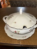 Soup terrene with lid and matching serving plate on wooden table, showing floral pattern and lid handle