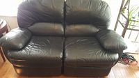Front view of black leather 2-seater recliner loveseat showing seat cushions and armrests with visible wear and a rip on right side.