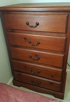 Front view of the 5 drawer solid wood dresser showing the antique-style metal handles and wood grain.