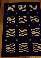 Photo showing the rectangular Ikea area rug featuring white wave-like patterns and round teal and orange motifs on a dark blue background laid flat on wood floor.