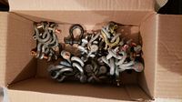A cardboard box filled with a variety of metal bell shackles of different sizes and finishes, including galvanized and black-coated steel, some with red-painted securing pins.