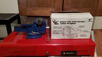 Photo of the blue Tool Tech 4 inch bench vice next to its original white packaging box on a red toolbox.