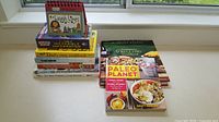 Photo showing a collection of 9 books including 8 cookbooks and 1 comic book calendar titled 'Laugh Lines'.