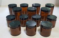 Front view showing all 14 amber glass jar candles with black lids, arranged in 3 rows, different sizes visible.